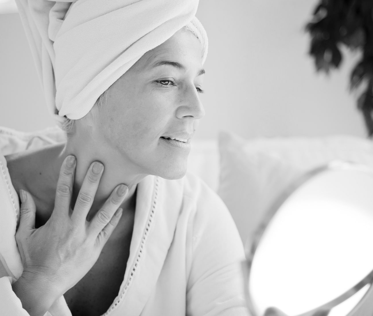 Woman with towel on head looking at neck on skin in the mirror, black and white mirror
